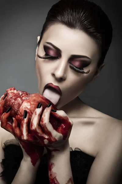 Schoonheid jonge vrouw likt bloed van menselijke hart — Stockfoto