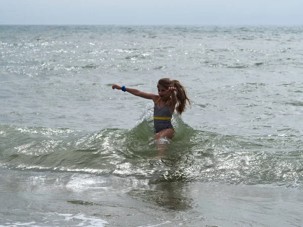 海の波に長い髪のストライプの水着の女の子が実行されます — ストック写真