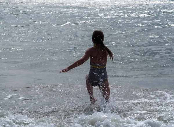 海の波に長い髪のストライプの水着の女の子が実行されます — ストック写真