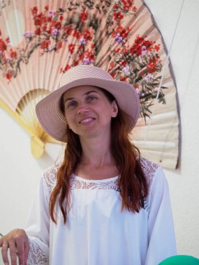 Beyaz elbiseli Ukraynalı bir kadın ve siyah saçlı bir plaj şapkası. Arka planda bir çiçek süsü var. 