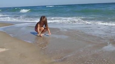 A lonely girl is playing on a deserted sea beach with foamy waves illuminated by the sun