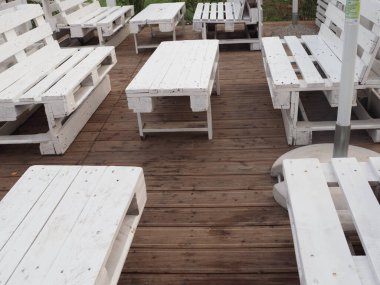 Deniz kıyısında bir kafenin içinde masaları ve beyaz paletlerden yapılma bankları olan insanlar yok.