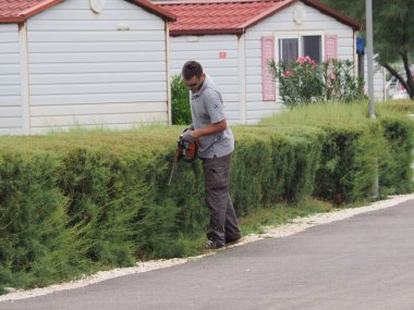 Trimming bushes near a house with a red roof