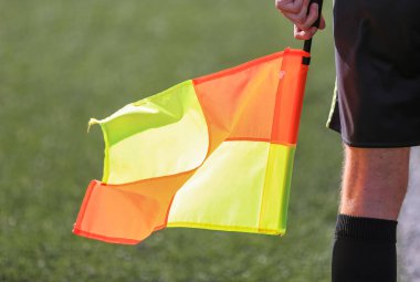 Siyah takım elbiseli bir futbol hakemi elinde bayrakla bir futbol sahasında duruyor.