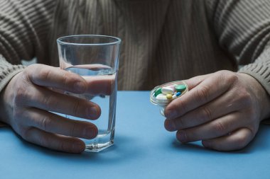 Adamın elinde bir bardak su ve hap var..