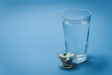 Mavi arka planda bir bardak su ve ilaç..