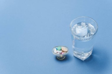 Tıbbi konsept - Mavi arka planda bir bardak su ve ilaç.
