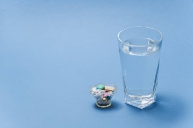 Tıbbi konsept - Mavi arka planda bir bardak su ve ilaç.