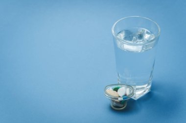 Tıbbi konsept - Mavi arka planda bir bardak su ve ilaç.