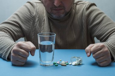 Adam yumruklarını sıkıyor, tıbbi hazırlıklar yapıyor ve önünde bir bardak su duruyor..