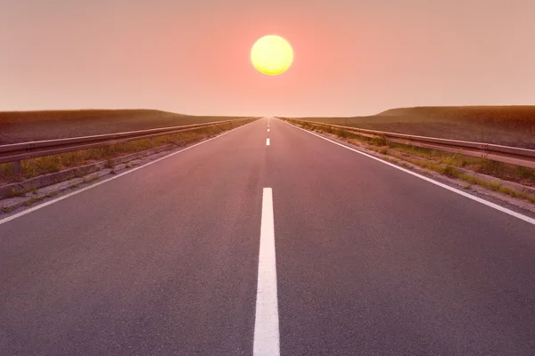 Guidare su strada vuota verso il sole al tramonto — Foto Stock