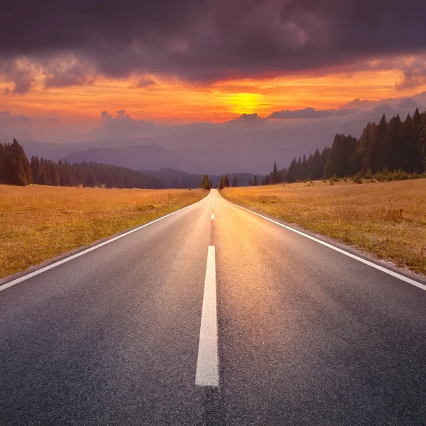 Guidare su una strada vuota verso il sole al tramonto — Foto Stock