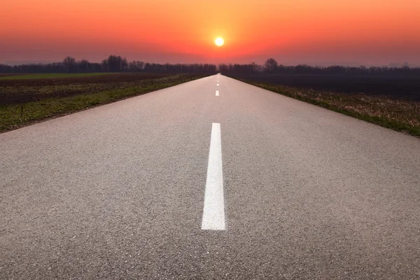 Driving on asphalt road towards the setting sun — Stock Photo, Image