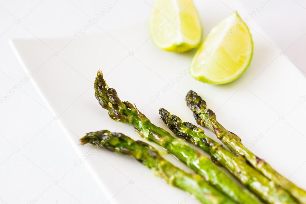 Green asparagus baked with olive oil and garlic. Served with two lime pieces on white plate.