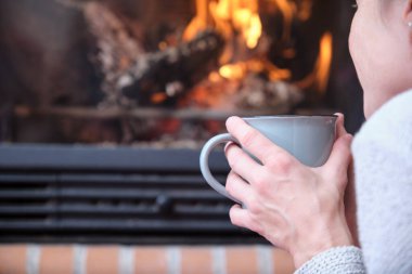 Rahatlamış kadın şöminenin önünde bir fincan kahve tutuyor..