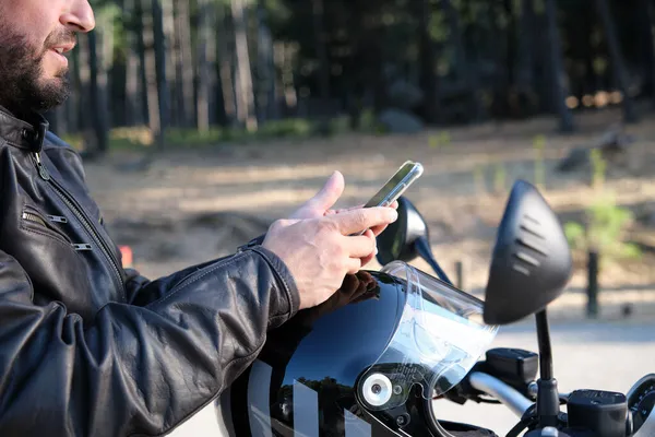 Um motociclista bonito usando telefone celular em uma estrada rural. — Fotografia de Stock