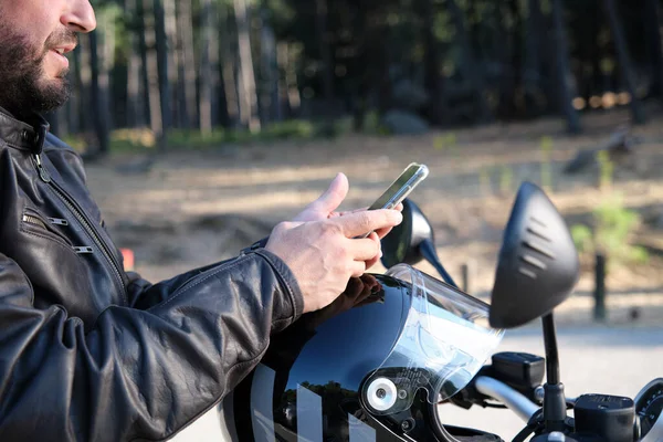 Kırsal bir yolda cep telefonu kullanan yakışıklı bir motorcu..