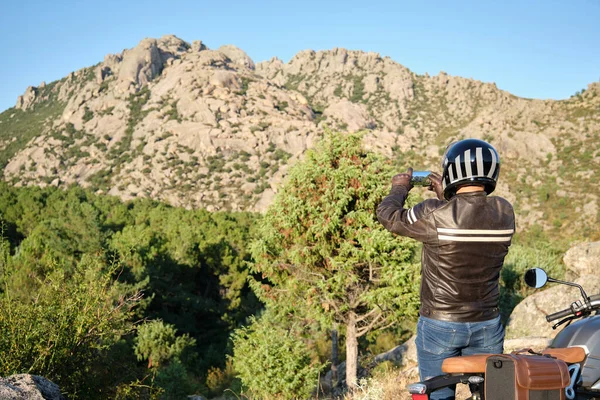 Motosiklet süren bir adam doğada akıllı telefonuyla fotoğraf çekiyor..