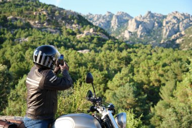 Motosikletçi doğada akıllı bir telefonla fotoğraf çekiyor..