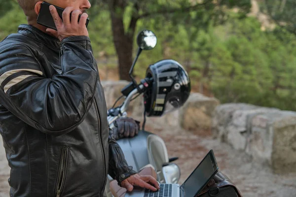 Цифровий кочівник з ноутбуком, що розмовляє по телефону під час подорожі на мотоциклі — стокове фото
