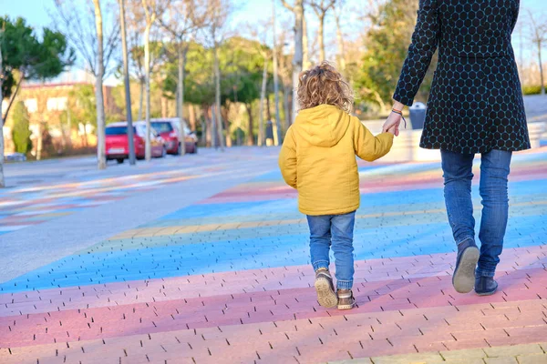 Una madre caminando de la mano con su hijo pequeño disfrutando de un momento de convivencia familiar en un parque. — Foto de Stock