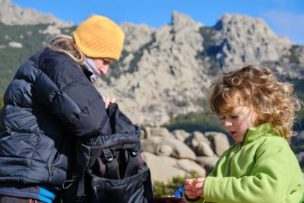 Una madre tomando comida de su mochila en las montañas con su hijo — Foto de Stock