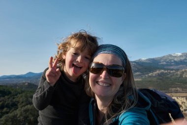 Bir anne ve oğlu doğada selfie çeker, çocuk yüzünü buruşturur ve dilini gösterir..