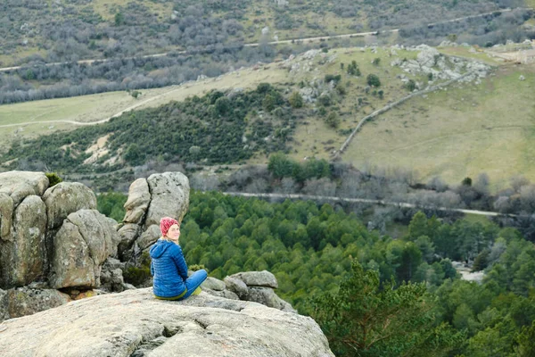 Uma mulher sentada à beira de um penhasco nas montanhas, olhando para a câmera. — Fotografia de Stock