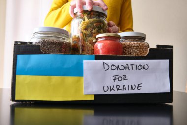 Tanınmayan bir kadın Ukraynalı mültecilere bağış yapmak için kavanozları bir kutuya koyuyor..