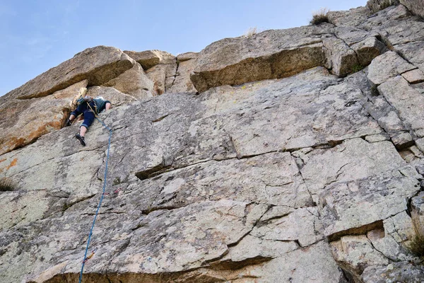 Man with climbing equipment climbing up a vertical rock wall.