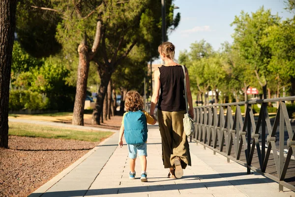 Rear view of schoolboy walking with mother on pavement