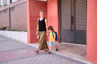 Parent and pupil of preschool. Woman and boy with backpack behind back. Beginning of lessons. First day of fall.