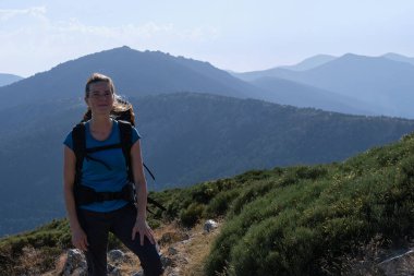 Sırt çantalı ve arka planda dağlar olan bir kadın yürüyüşçü.