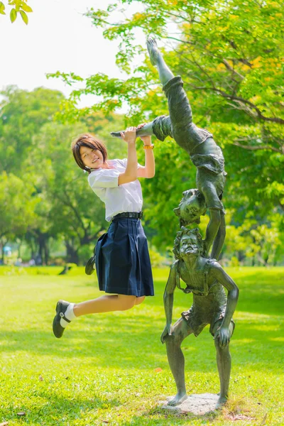 Söt thailändska skolflicka hoppar med en staty i parken — Stockfoto