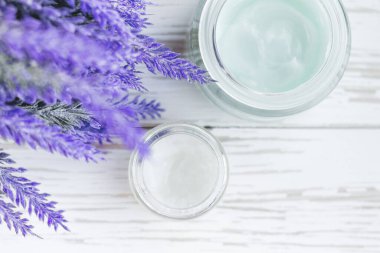 Beyaz ahşap arka planda çiçekli kozmetik krem kabı. Yüz kremi