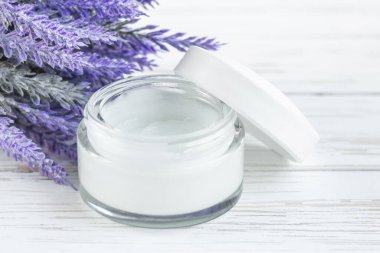 Beyaz ahşap arka planda çiçekli kozmetik krem kabı. Yüz kremi