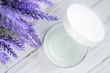 Beyaz ahşap arka planda çiçekli kozmetik krem kabı. Yüz kremi