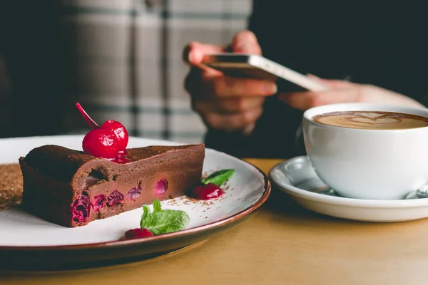 Girl with a mobile phone, coffee and cake in a cafe. Female hands holding a smartphone. The girl is chatting in a cafe, check social media or chatting on mobile