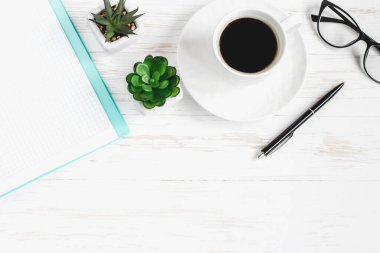 Not defteri, kalem, bardaklar, bitkiler sulu, beyaz ahşap bir masada bir fincan kahve, düz yatak, üst manzara. Ofis masası, iş yeri.