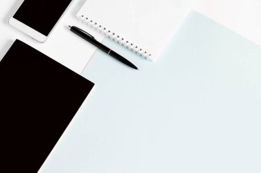 Not defteri, kalem, akıllı telefon, ofis aletleri, açık mavi arka plan, fotokopi alanı, üst görünüm. Ofis aksesuarlarının kompozisyonu sayfanın solunda.