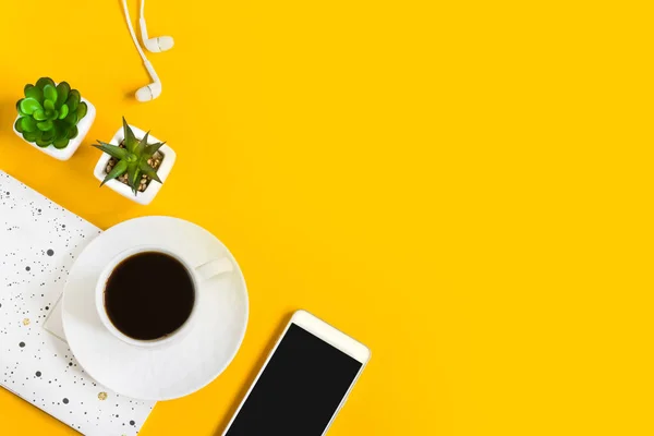 Morning coffee, notebook, mobile phone, plants on a yellow background. Copy space. Top view. Business yellow background