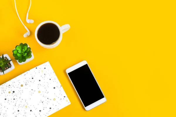 Morning coffee, notebook, mobile phone, plants on a yellow background. Copy space. Top view. Business yellow background