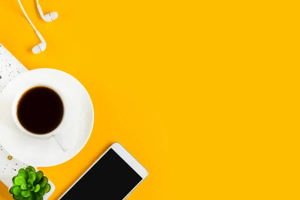 Morning coffee, notebook, mobile phone, plants, headphones on a yellow background. Copy space. Top view. Business yellow background. Flat lay, concepts ideas