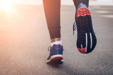 Sabah koşusu. Kırsal bir yolda koşan genç bayan gün batımında siyah tabanlı mavi spor ayakkabılarla koşuyor. Sağlıklı bir yaşam tarzı. Spor eğitimi konsepti