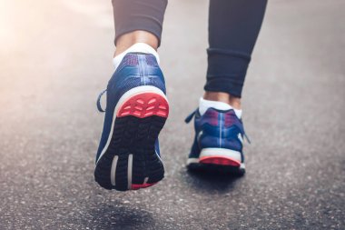 Sabah koşusu. Kırsal bir yolda koşan genç bayan gün batımında siyah tabanlı mavi spor ayakkabılarla koşuyor. Sağlıklı bir yaşam tarzı. Spor eğitimi konsepti