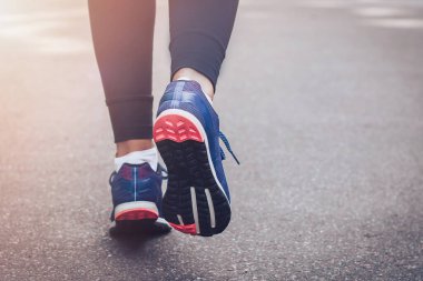 Sabah koşusu. Kırsal bir yolda koşan genç bayan gün batımında siyah tabanlı mavi spor ayakkabılarla koşuyor. Sağlıklı bir yaşam tarzı. Spor eğitimi konsepti