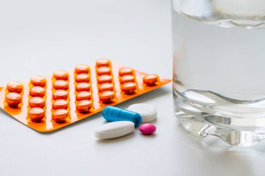 Su toplayan haplar, kapsüller, beyaz arka planda bir bardak su. Soğuk algınlığı, vitamin ve sağlık kompleksinin tedavisi için hazırlıklar
