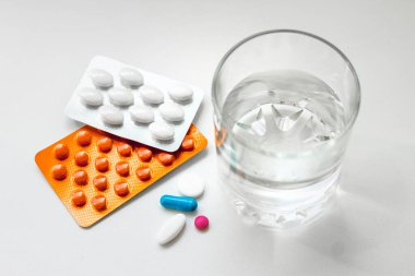 Su toplayan haplar, kapsüller, beyaz arka planda bir bardak su. Soğuk algınlığı, vitamin ve sağlık kompleksinin tedavisi için hazırlıklar