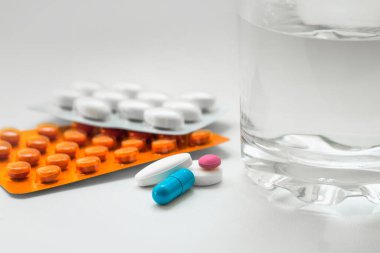 Su toplayan haplar, kapsüller, beyaz arka planda bir bardak su. Soğuk algınlığı, vitamin ve sağlık kompleksinin tedavisi için hazırlıklar