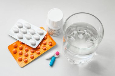 Su toplayan haplar, kapsüller, beyaz arka planda bir bardak su. Soğuk algınlığı, vitamin ve sağlık kompleksinin tedavisi için hazırlıklar